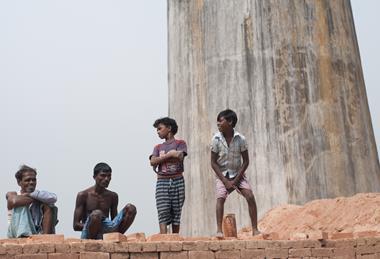 工人和他们的家人站在砖厂的一堆砖上，他们在那里工作，并呆在艰苦和不健康的条件下