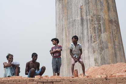 Workers and their family members standing on stacks of bricks in a brick factory where they work and stay under tough and unhealthy conditions