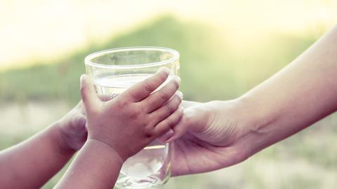 Woman hand giving glass of fresh water to little child girl in the park